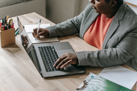 Woman with laptop writing in a notebook